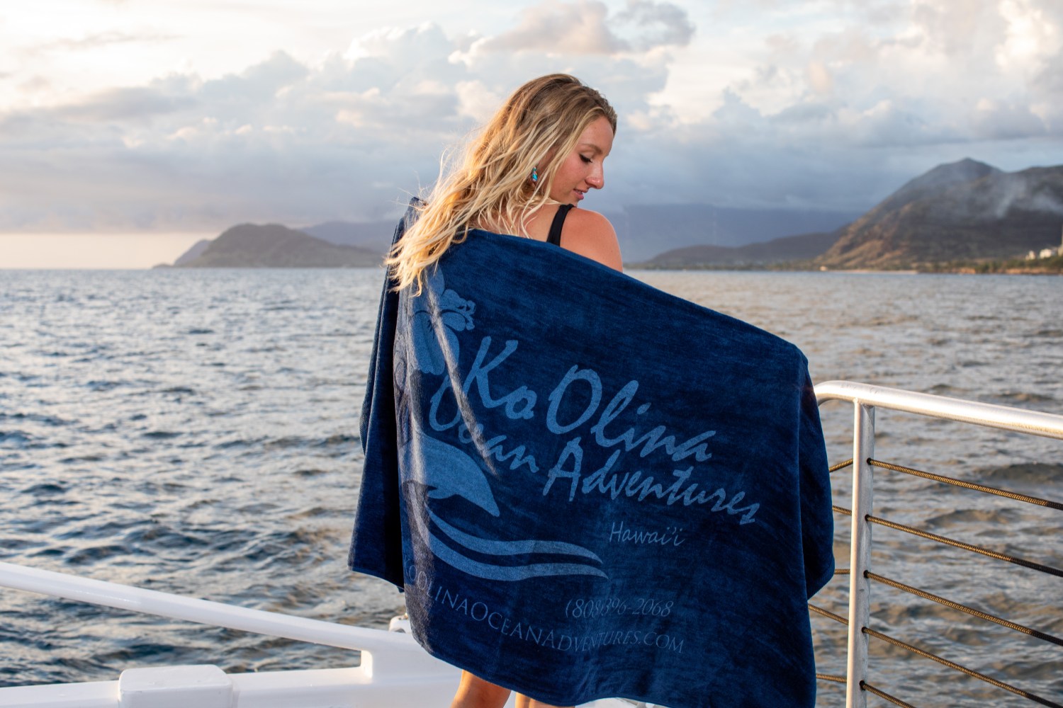 Woman on boat wrapped in Ko Olina towel overlooking ocean and mountains.