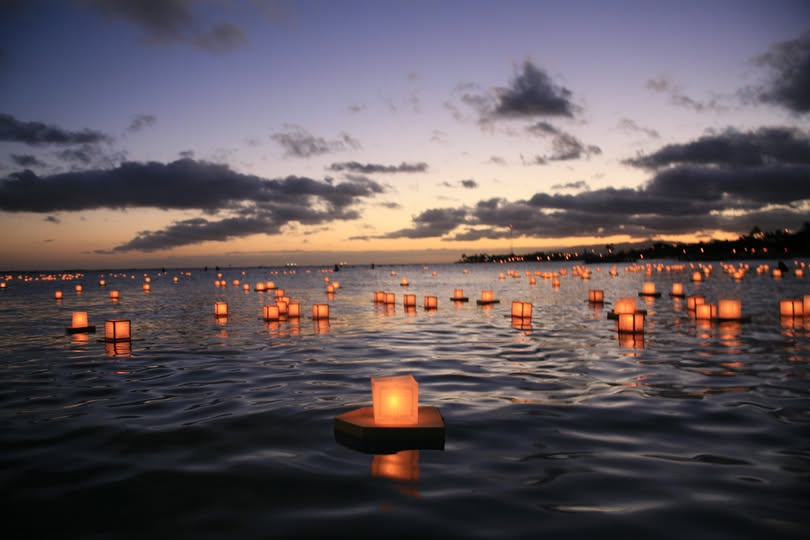 Floating lanterns on water at sunset with a cloudy sky.