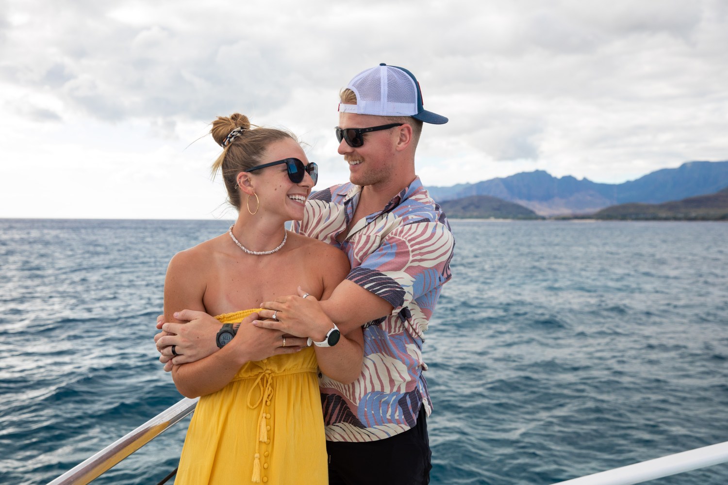 Couple embracing on a boat, ocean and mountains in background.