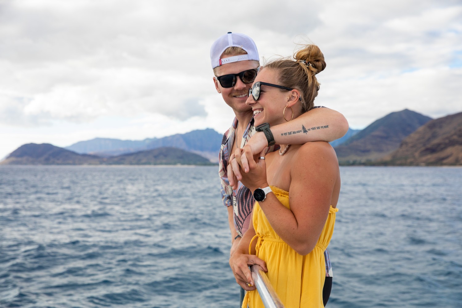 Couple smiling on a boat with mountains and sea in the background.