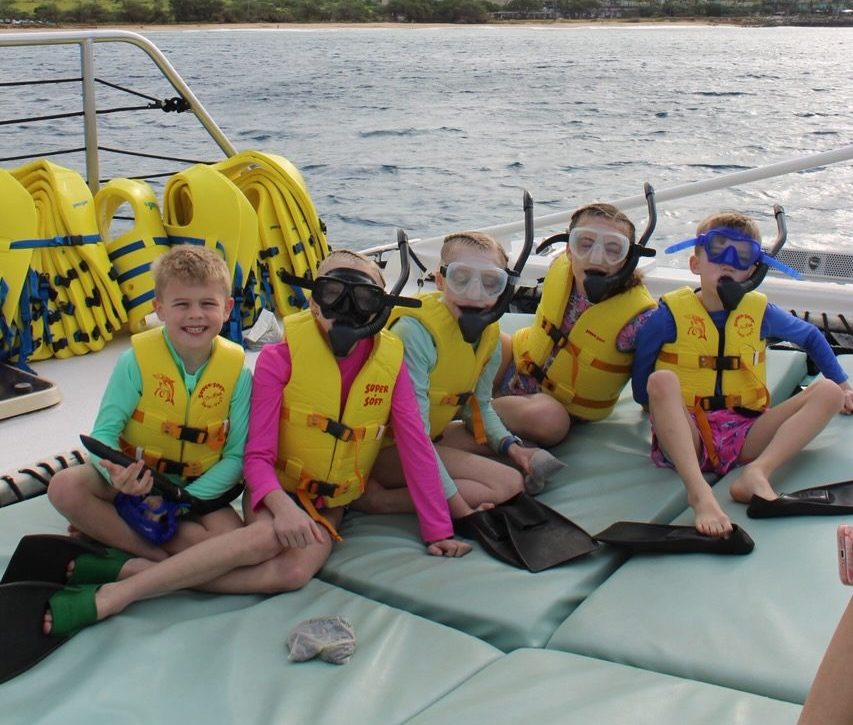 Kids in snorkel gear on a boat near a green hillside.