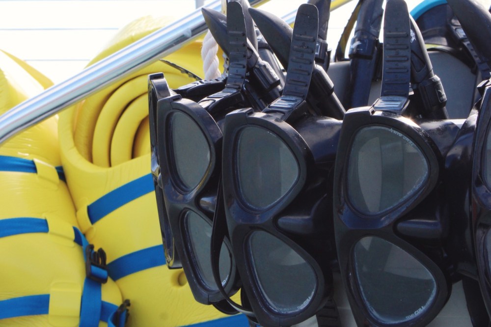 Stacked snorkeling masks and yellow life jackets on a rack.